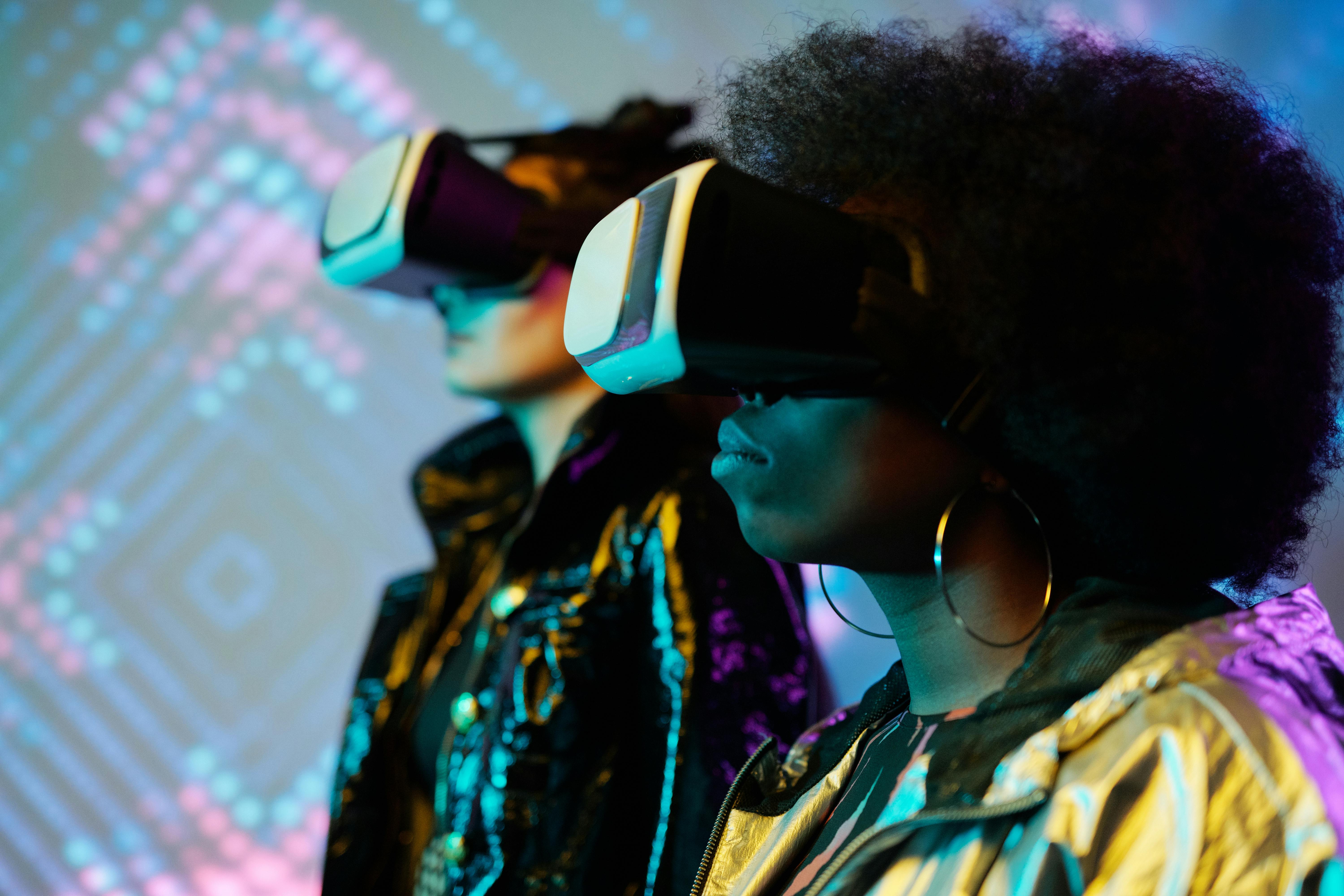 Two people wearing virtual reality headsets illuminated by colorful digital light patterns.
