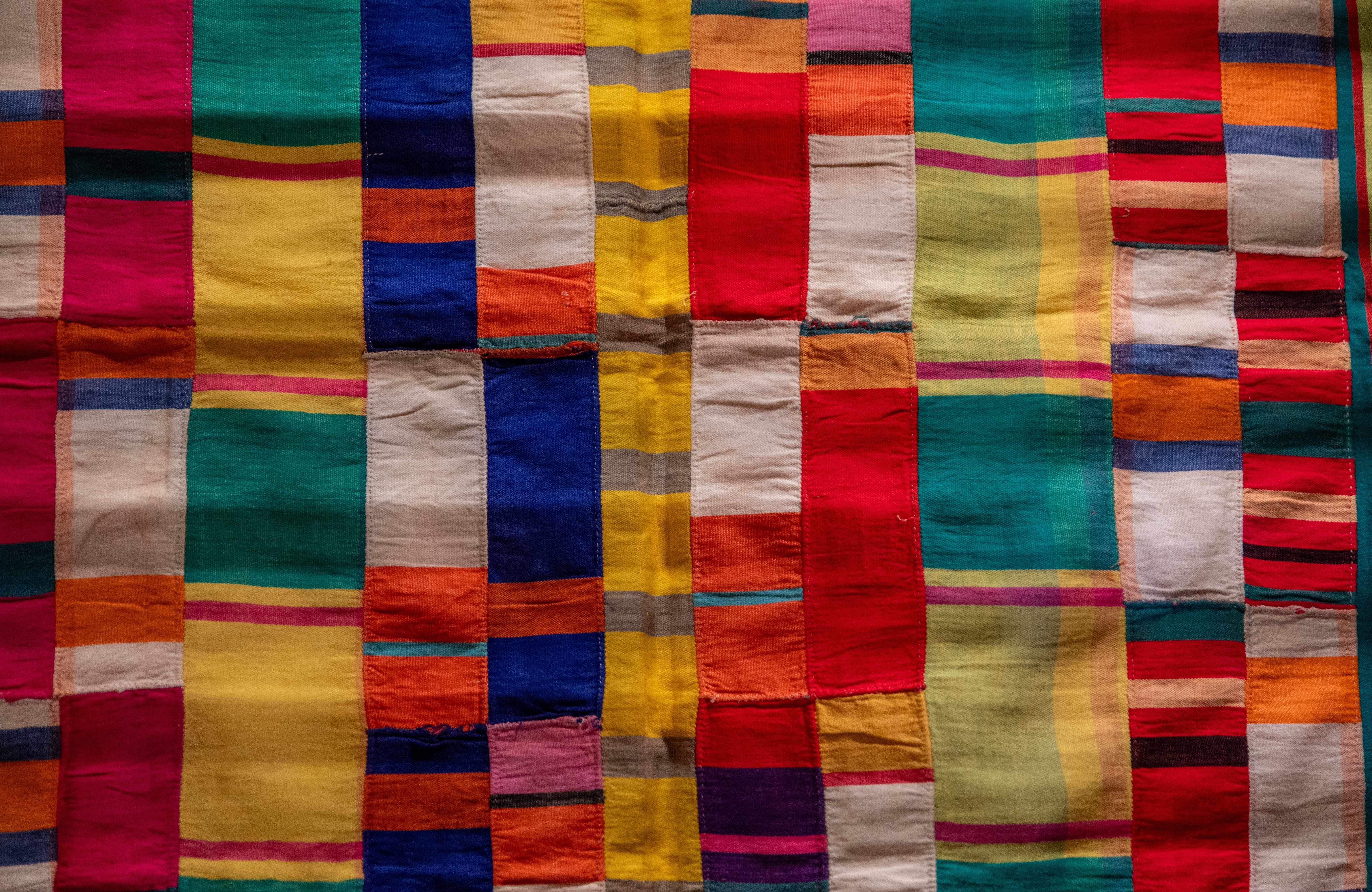 Colorful patchwork quilt with vertical and horizontal stripes in red, blue, yellow, orange, purple, and green.